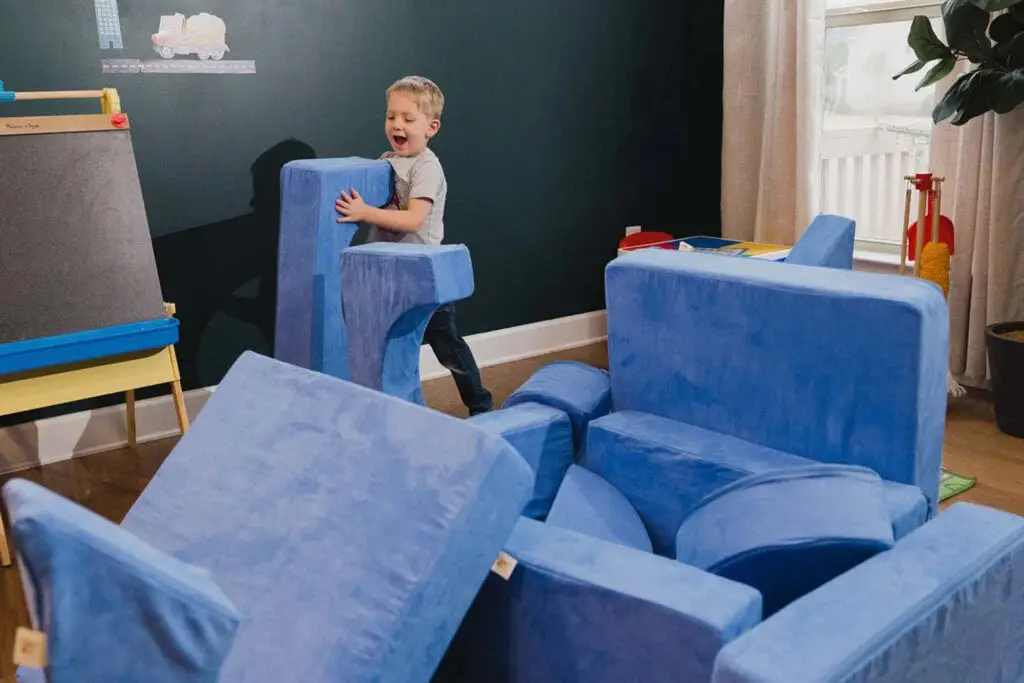 Young child building and playing on a blue modular foam play sofa in a living room.